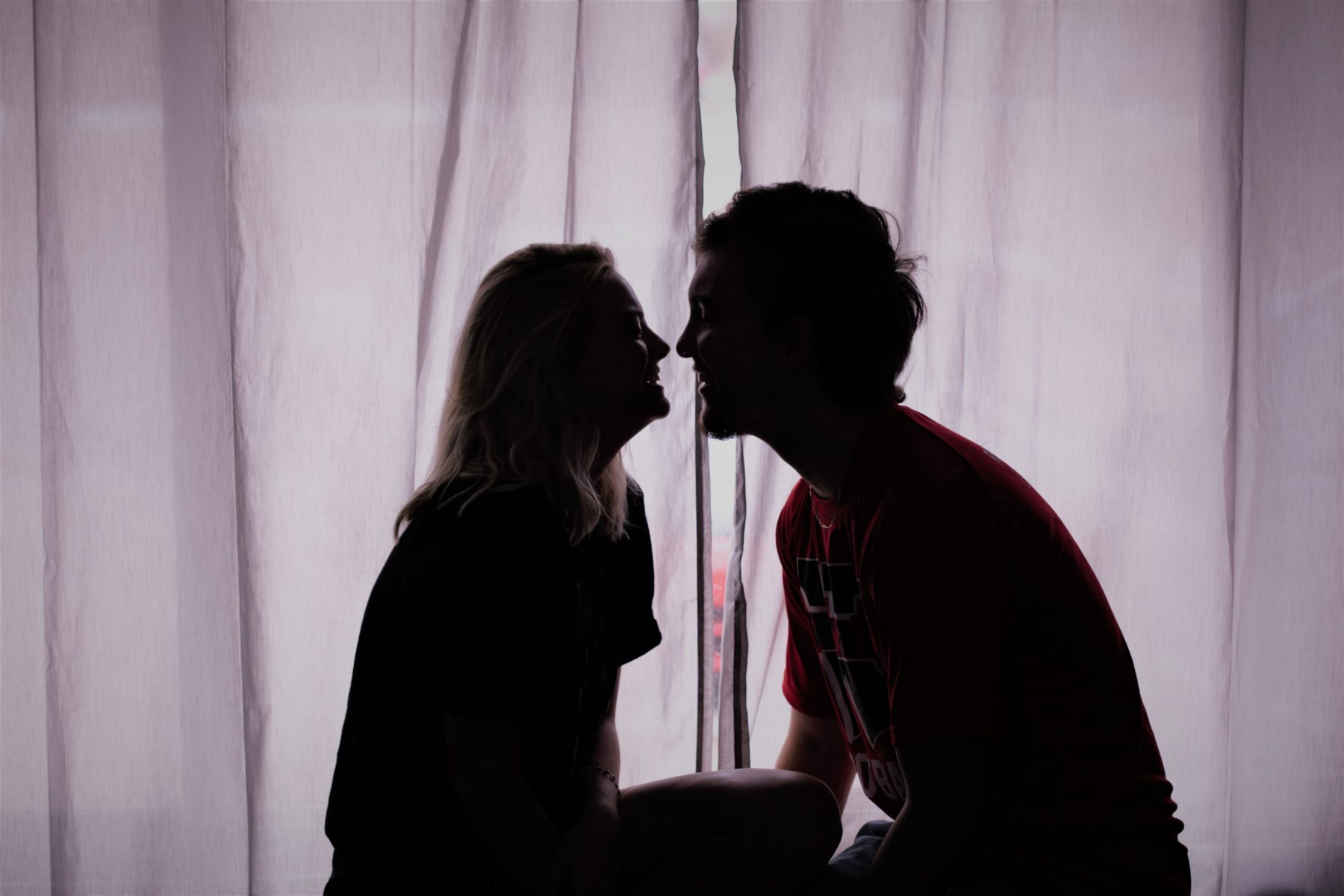 Husband And Wife sitting on a bed in front of curtains